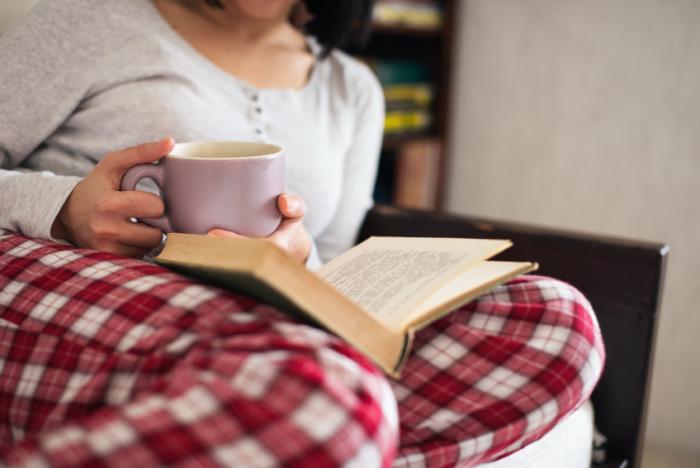 Жена с чаша четене в пижама.