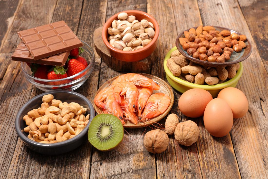 Aliments d'allergie disposés sur la table en bois, y compris les noix de cajou, les noix de pécan, les noisettes, les amandes. chocolat, fraises, crustacés, noix, œufs et kiwi.