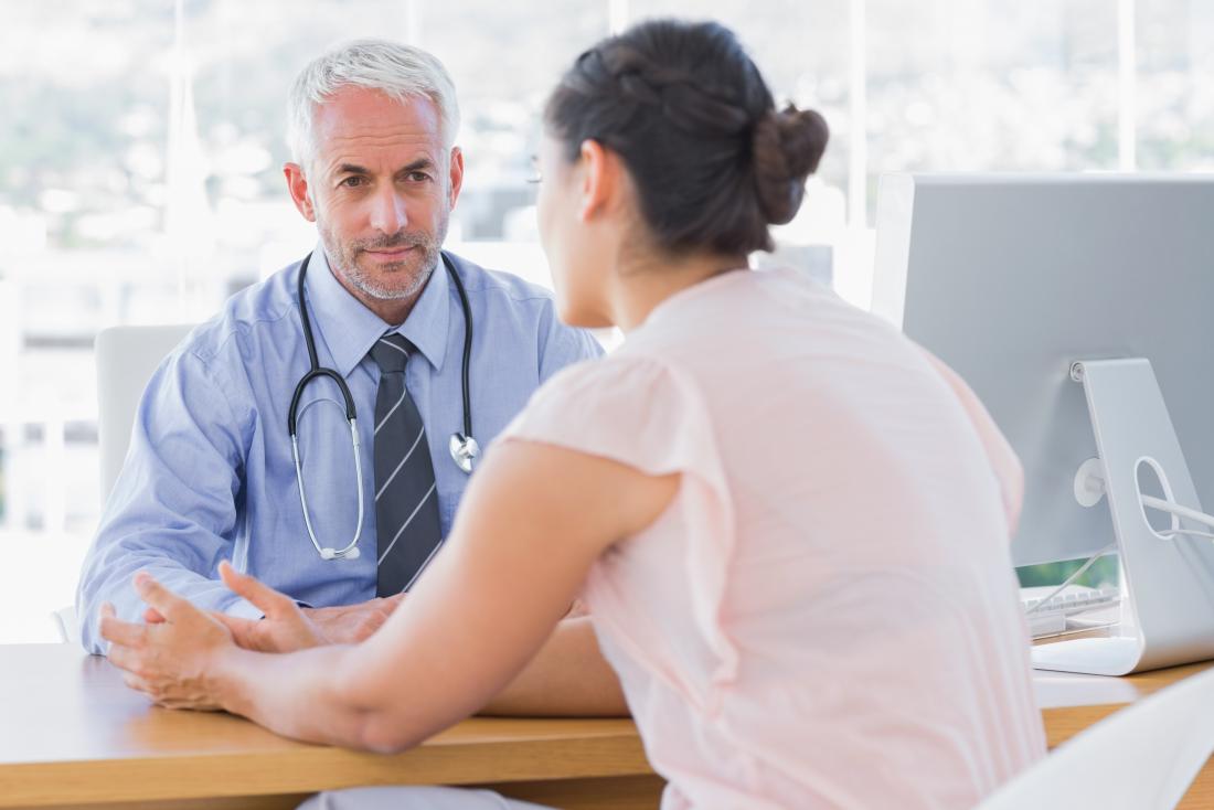 Weiblicher Patient, der mit männlichem Doktor in seinem Büro spricht.