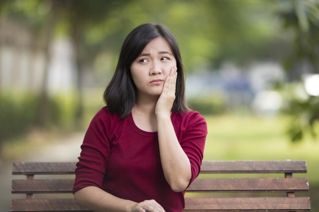 Mulher que senta-se em um banco de parque que prende seu mordente na dor, por causa de uma dor de dente ou de uma língua dorido.