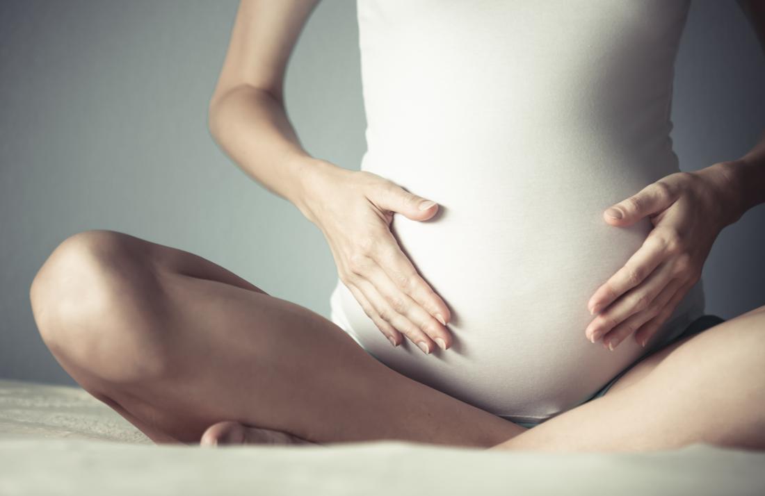 Femme enceinte représentant le vagin sent comme l'ammoniac assis jambes croisées sur le lit.