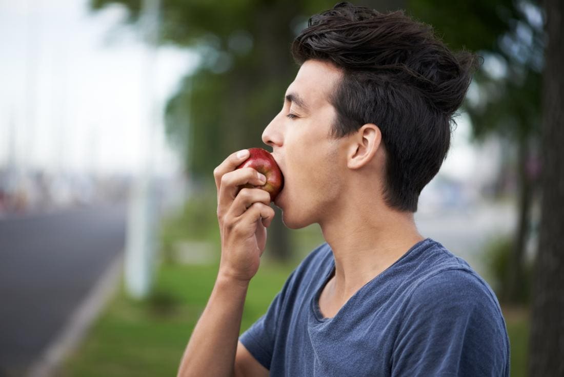 Người đàn ông ăn một quả táo bên ngoài.