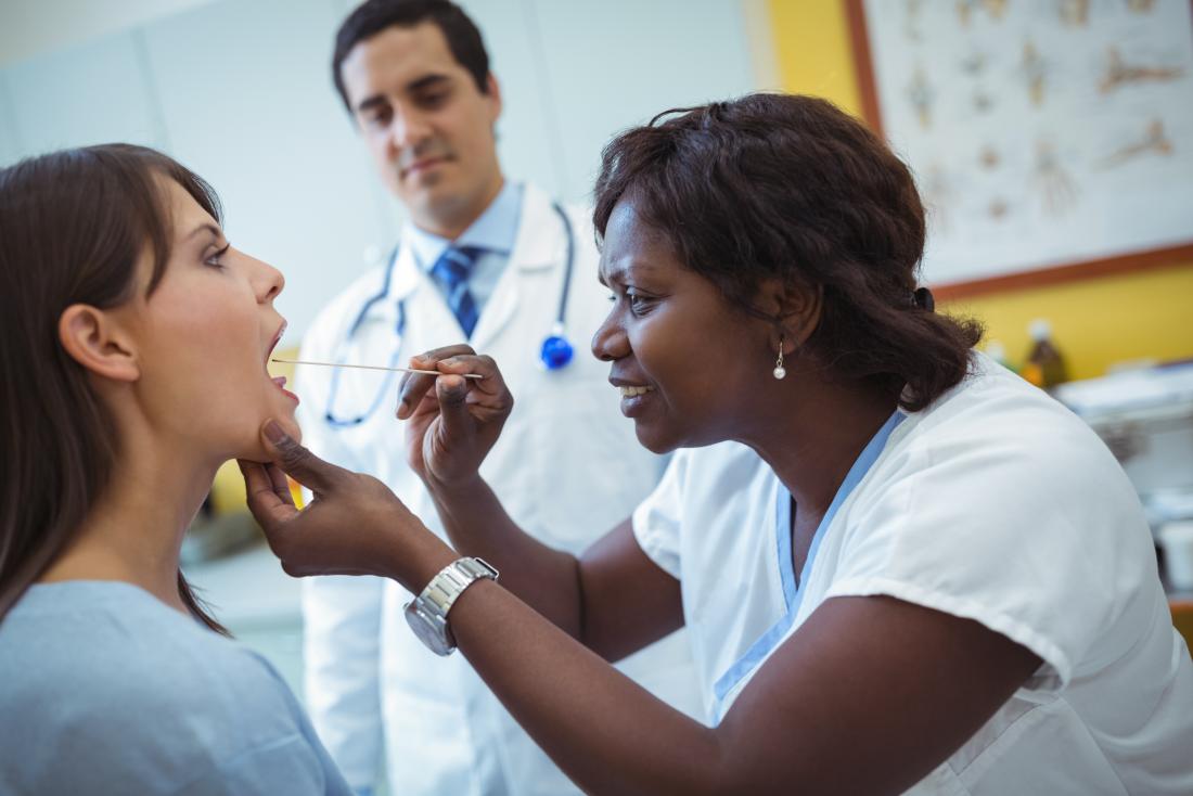 Doutor inspecionando pacientes garganta com outro médico, usando descompressor de língua.