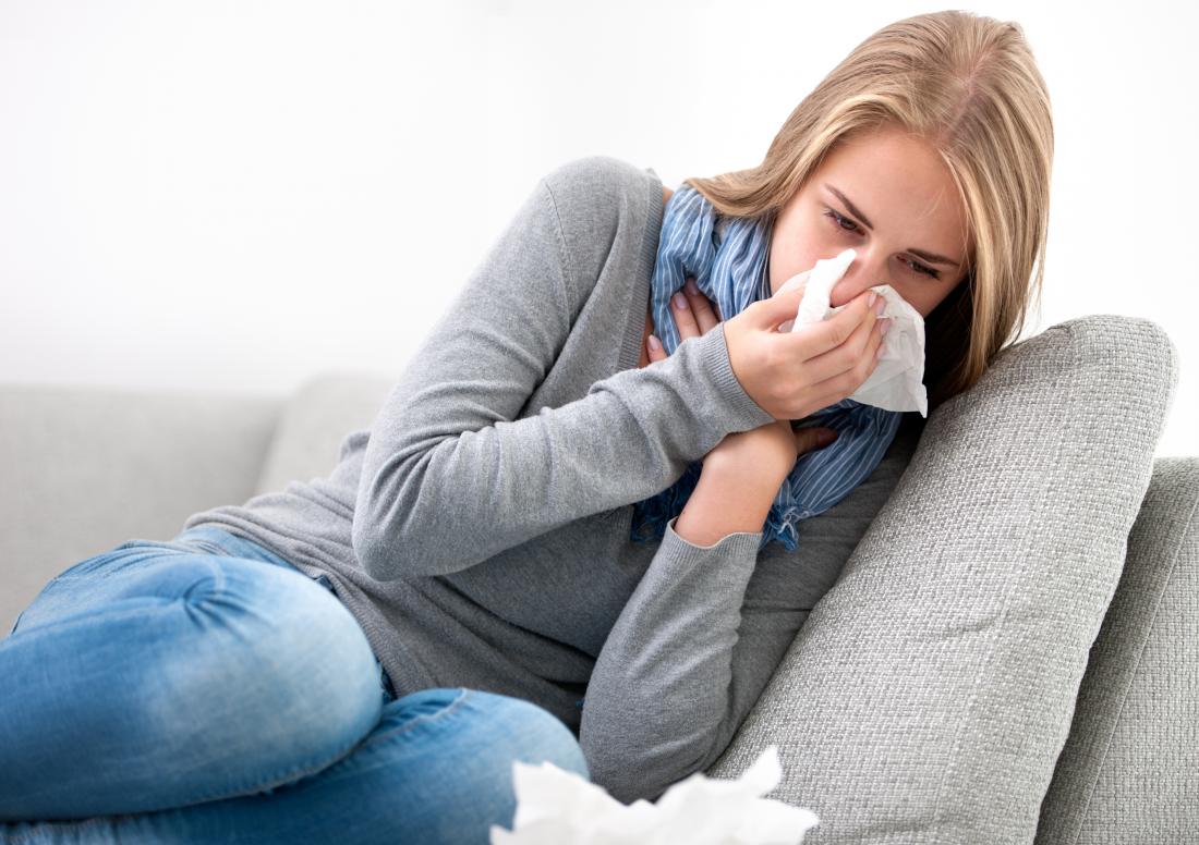Donna malata con l'infezione che soffia il naso seduto sul divano.
