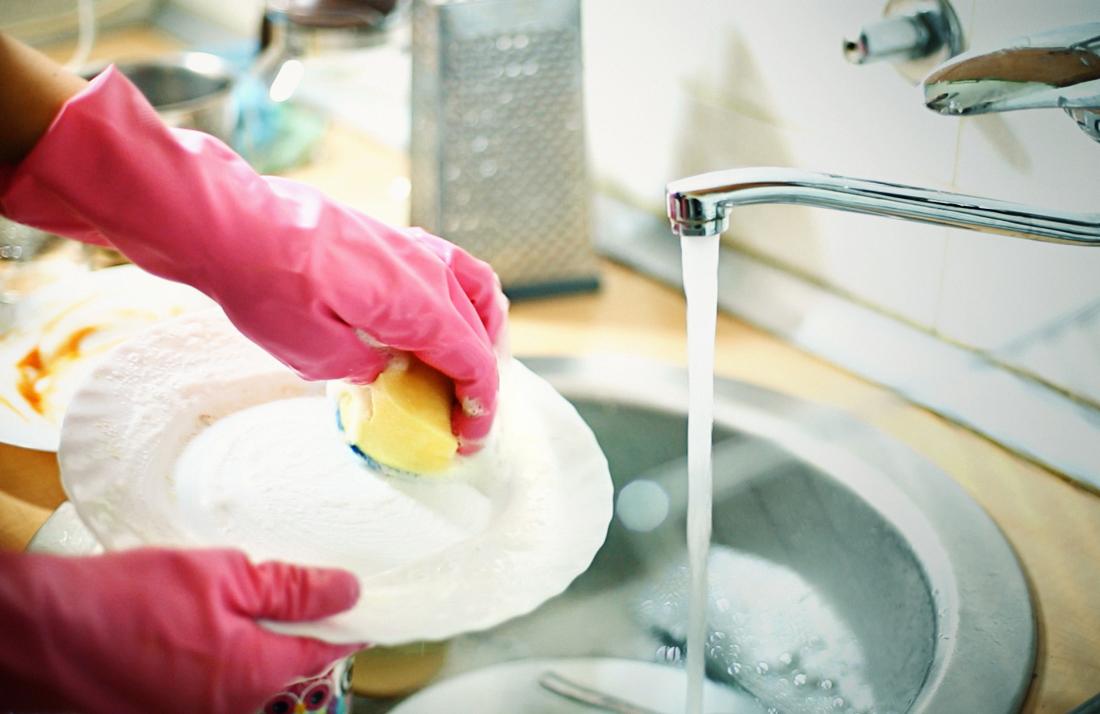 Kuru ellerden kaçınmak için bulaşık yıkarken lastik eldiven kullanan kişi