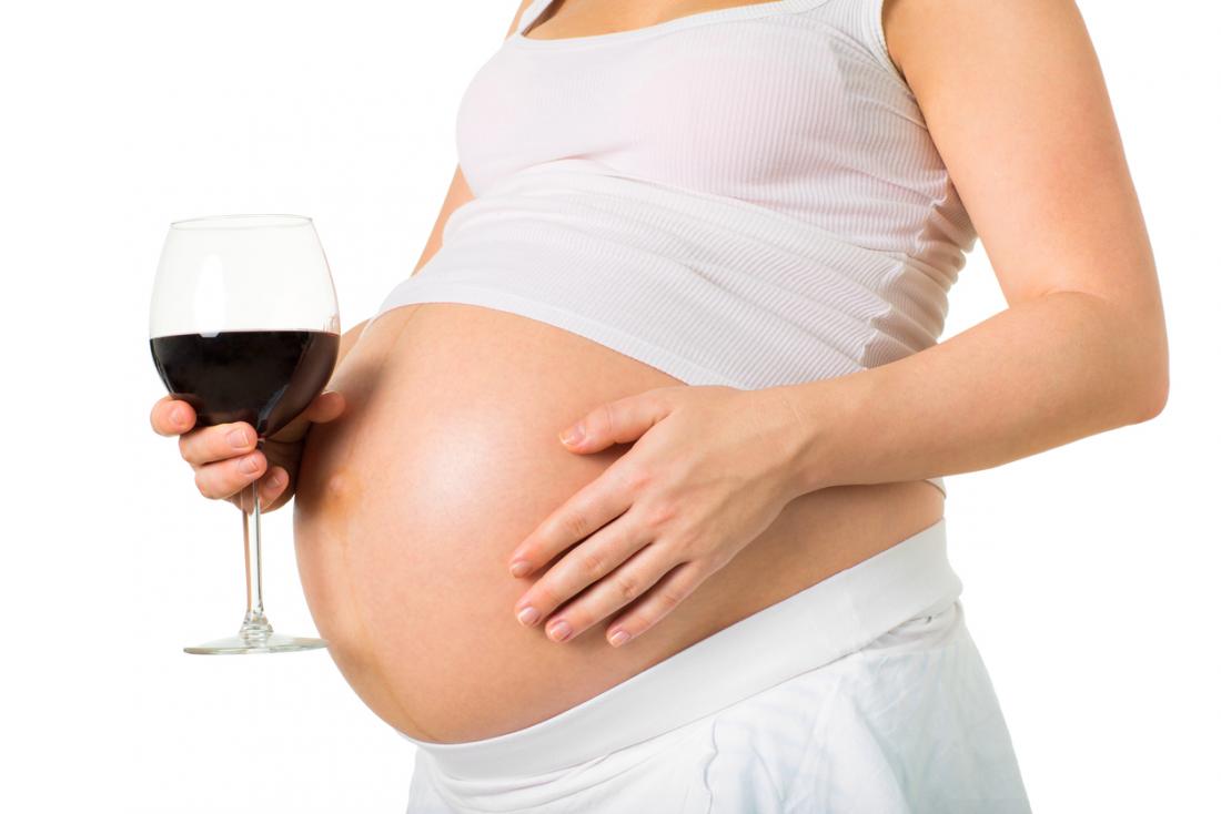 eine schwangere Frau, die ein Glas Wein anhält