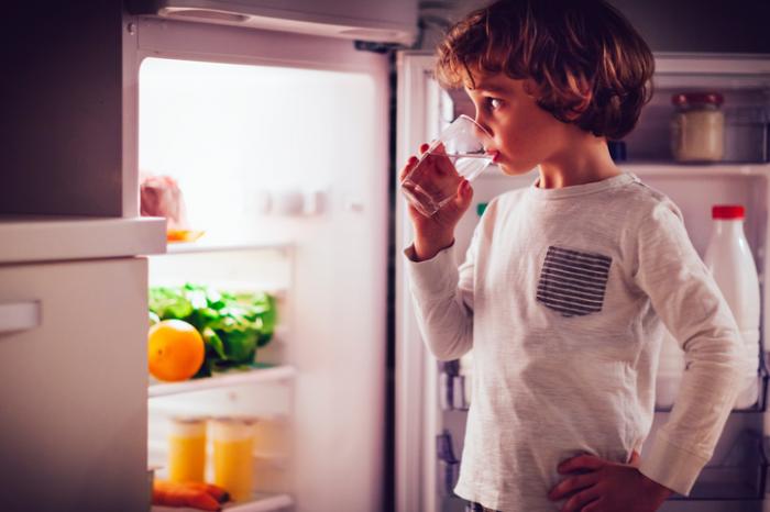 Một cậu bé uống nước bên cạnh một tủ lạnh mở.