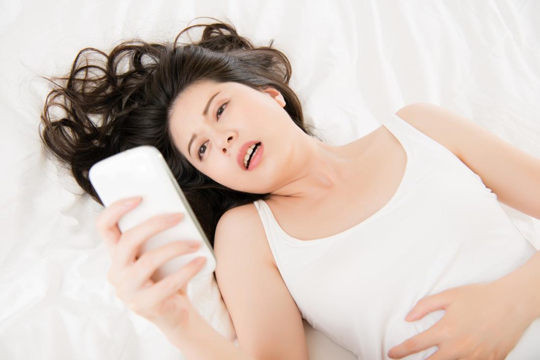 Frau mit den starken Bauchschmerzen, die Telefon betrachten