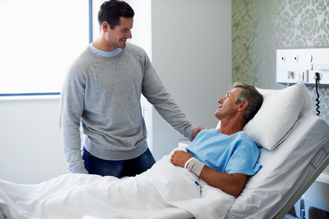 Homme récupérant d'une intervention chirurgicale dans un lit d'hôpital avec un visiteur masculin.