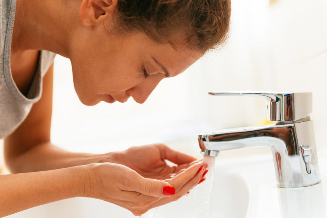 Жена, събираща вода в ръцете си от кранчето в мивката, за да измие лицето.