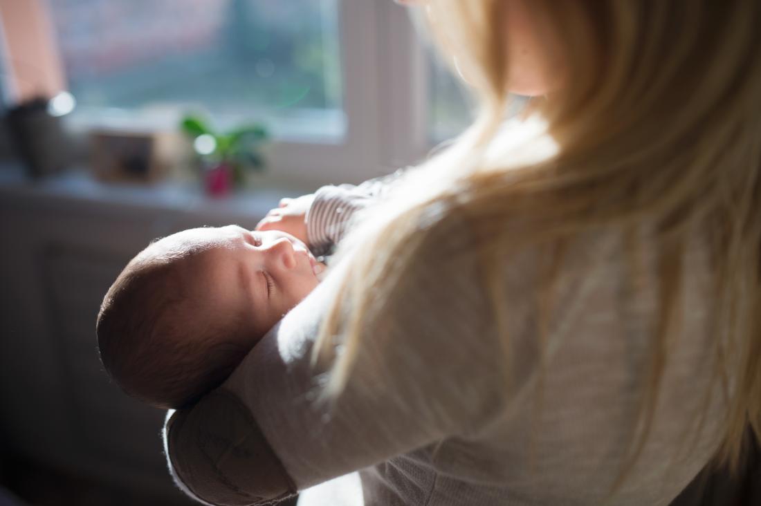 Хидранцефалия в главата на бебето, подчертана от слънчевата светлина, държана в ръцете на жената.